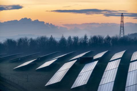 An image of solar panels in a field at sunset